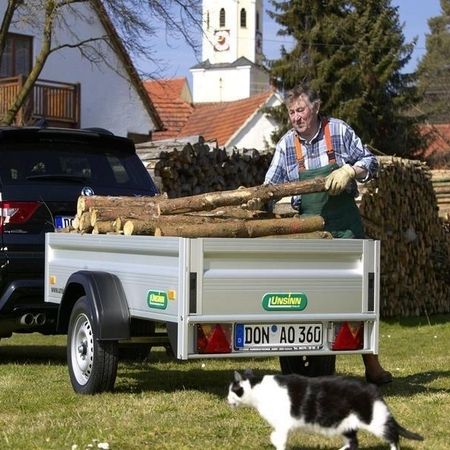 Aufnahme eines Menschen, der einen Kastenanhänger mit Rohholz beläd