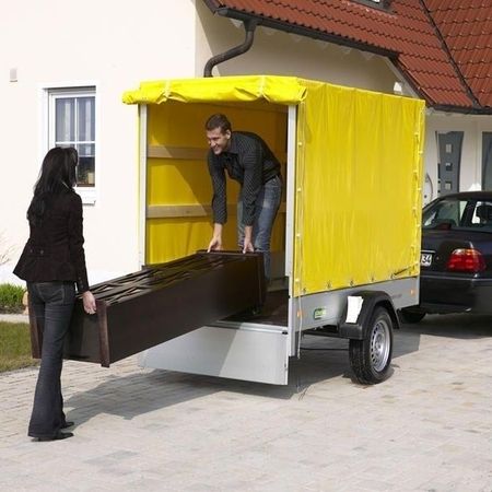 Aufnahme von 2 Menschen, die gerade etwas in einem Kastenanhänger verladen